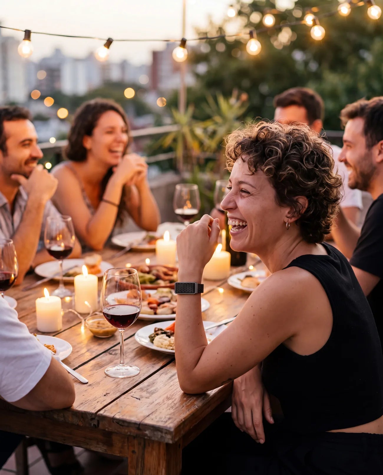 Mujer riéndose en una cena con amigos, con la pulsera AURA